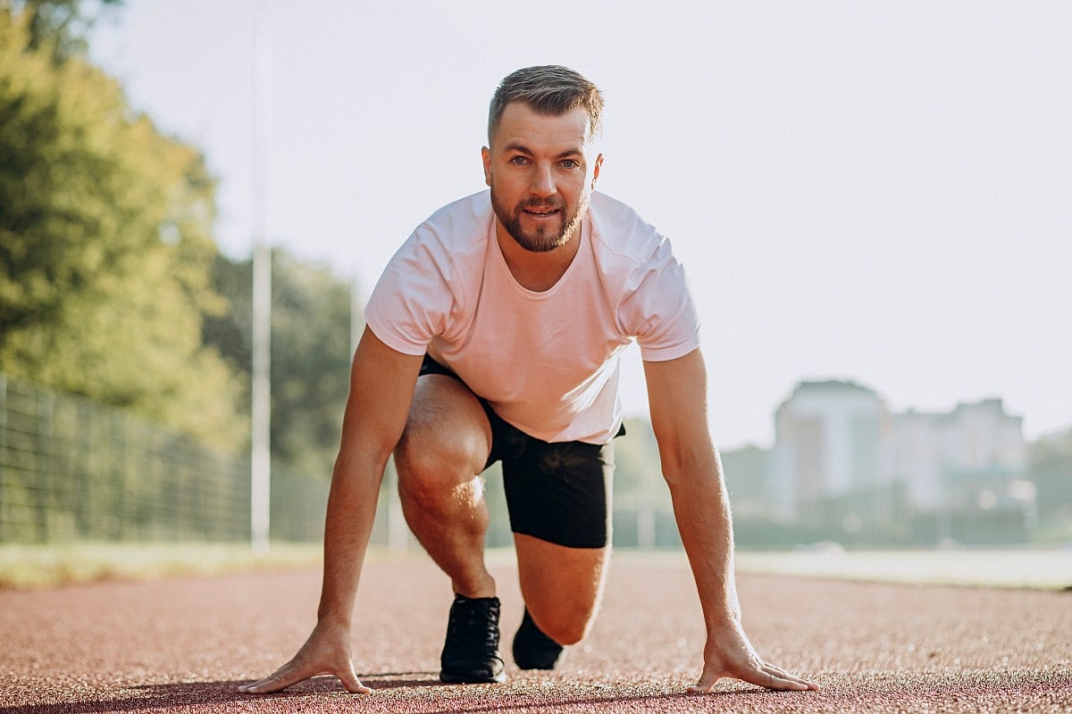 Un hombre se encuentra en la posición de salida en una pista de atletismo, listo para prevenir la disfunción eréctil mediante el ejercicio.