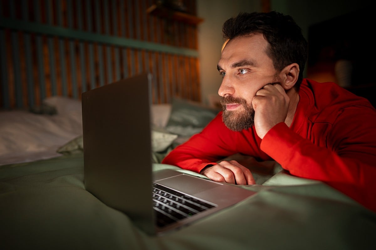 Un hombre ve pornografía en línea en su cama.